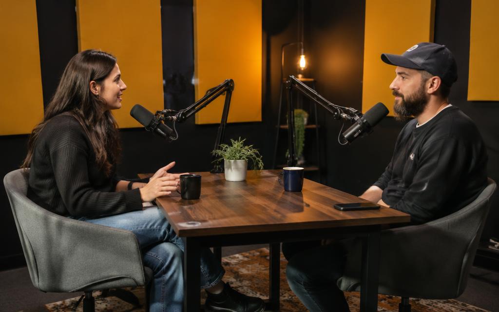 Two people recording a podcast across a table with microphones